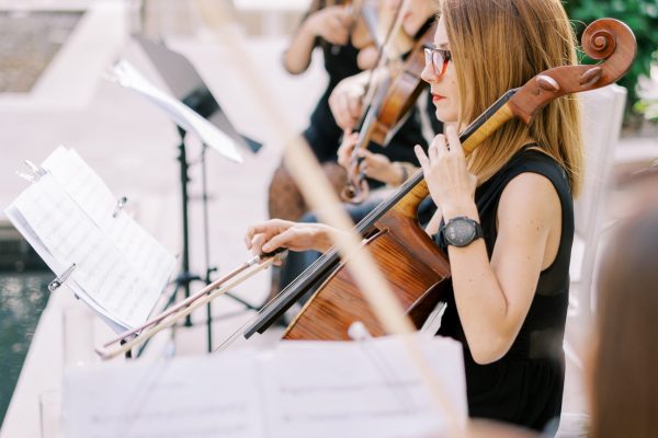 Cellist with violinists plays in the garden sitting on chairs in front of music stands. High quality photo