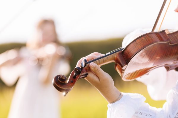 little girl is playing violin outdoor with garden in the background on sunny summer day. Image with selective focus and copy space