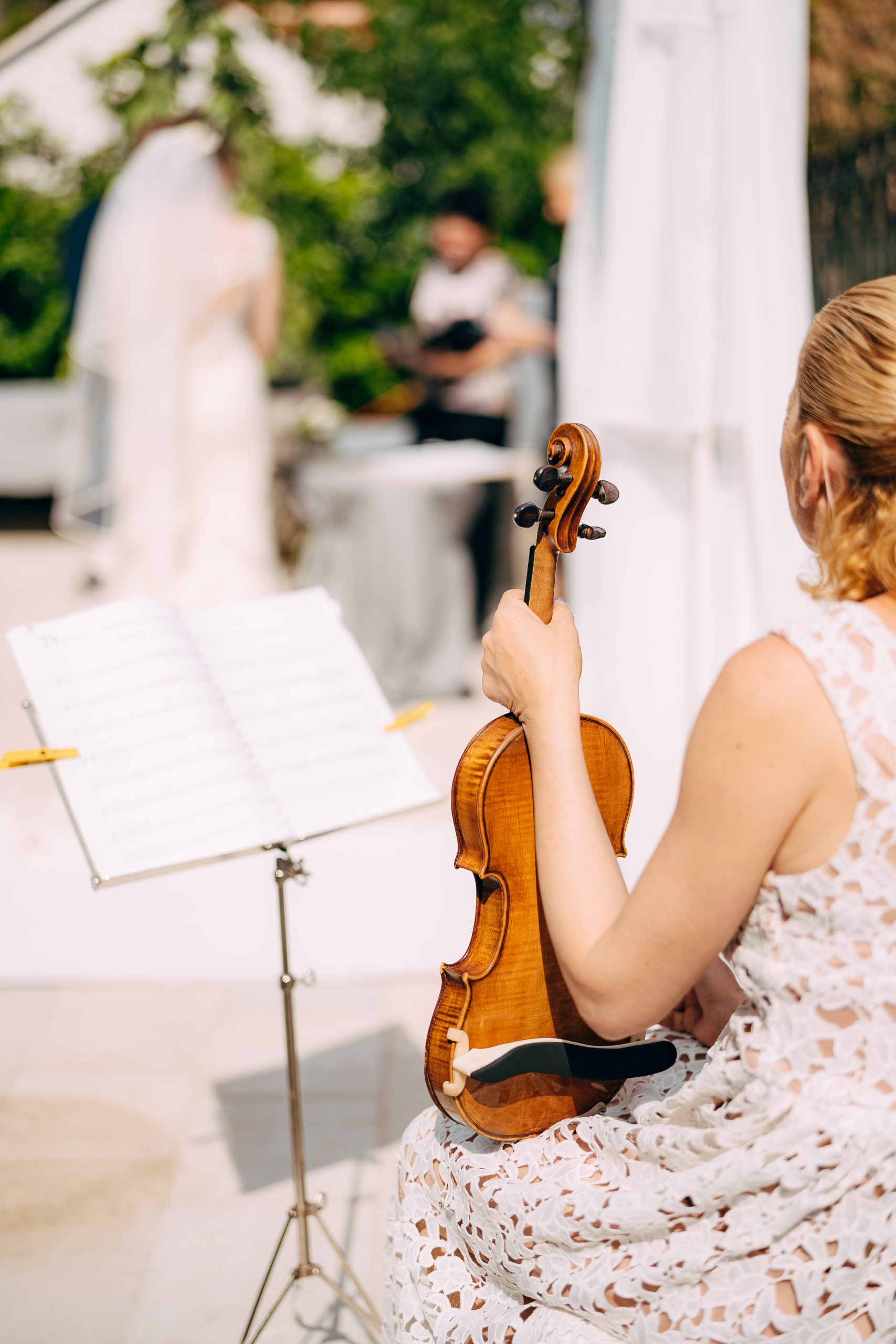 Girl musician sits near the music stand and holds a violin during the wedding ceremony, back view . High quality photo